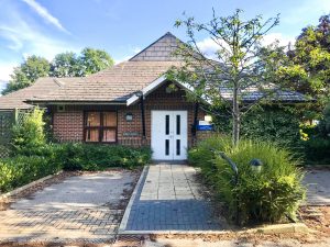 red brick building exterior with a white door, carpark in front and green hedge