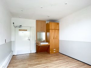 a wooden floored bedroom with white walls, a wooden cupboard and sink