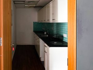 a narrow kitchen with white cabinets and teal tiles above the counter