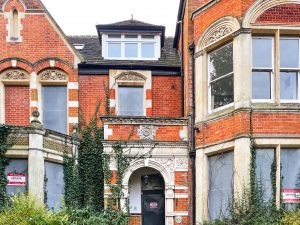 a red brick building exterior with windows, an arch, vines creeping up the walls and some white brick decorations