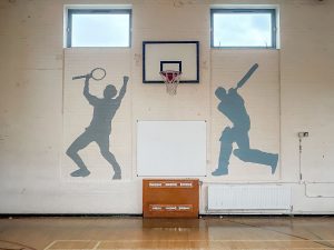 basketball hoop on a indoor white wall next to images of a baseball and tennis player