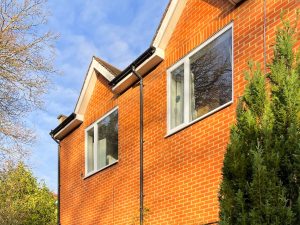 the outside of a red brick building with sloping roofs, two windows in the walls and a tree in front