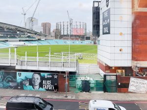 a green field with a white building on the side reading 'the oval'. the field is the Oval Cricket Ground in London