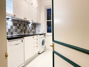 door on the right hand side of the photo with green detailing and a golden handle, white kitchen inside with a washing machine and black tiling