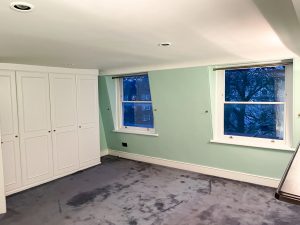 bedroom with turquoise walls, white cupboards and a carpeted floor