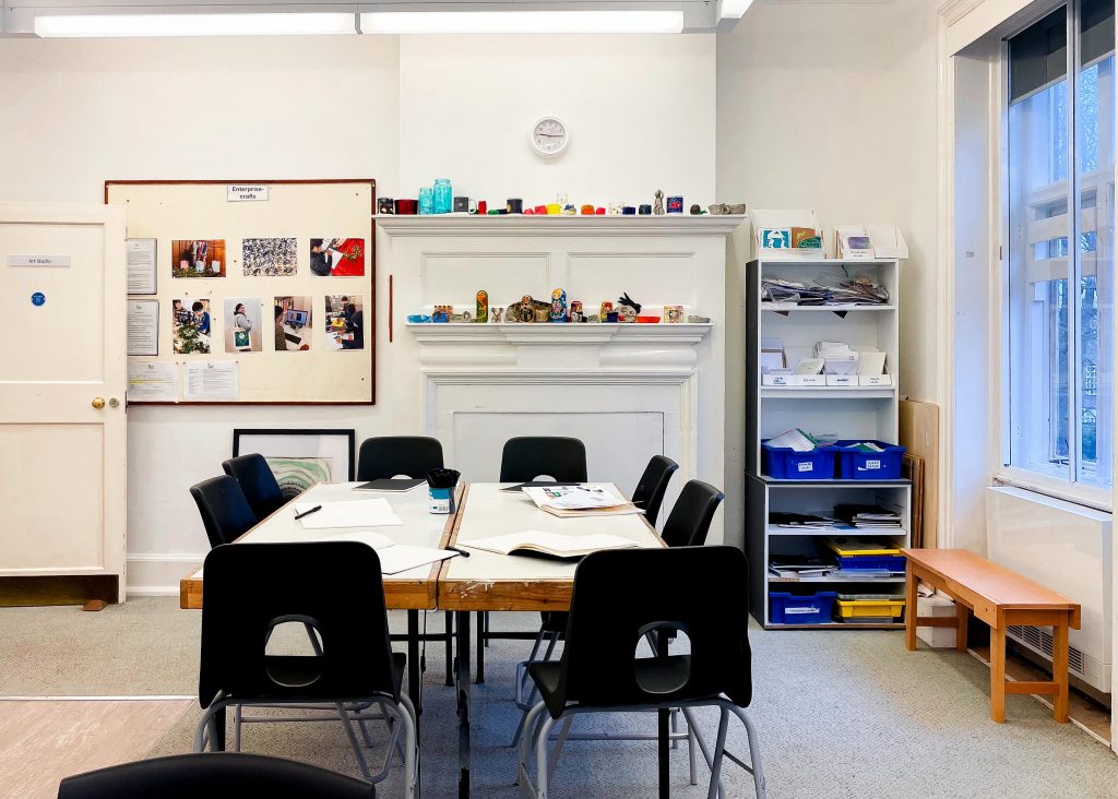 two desks next to each other are surrounded by black chairs with art books on the tables