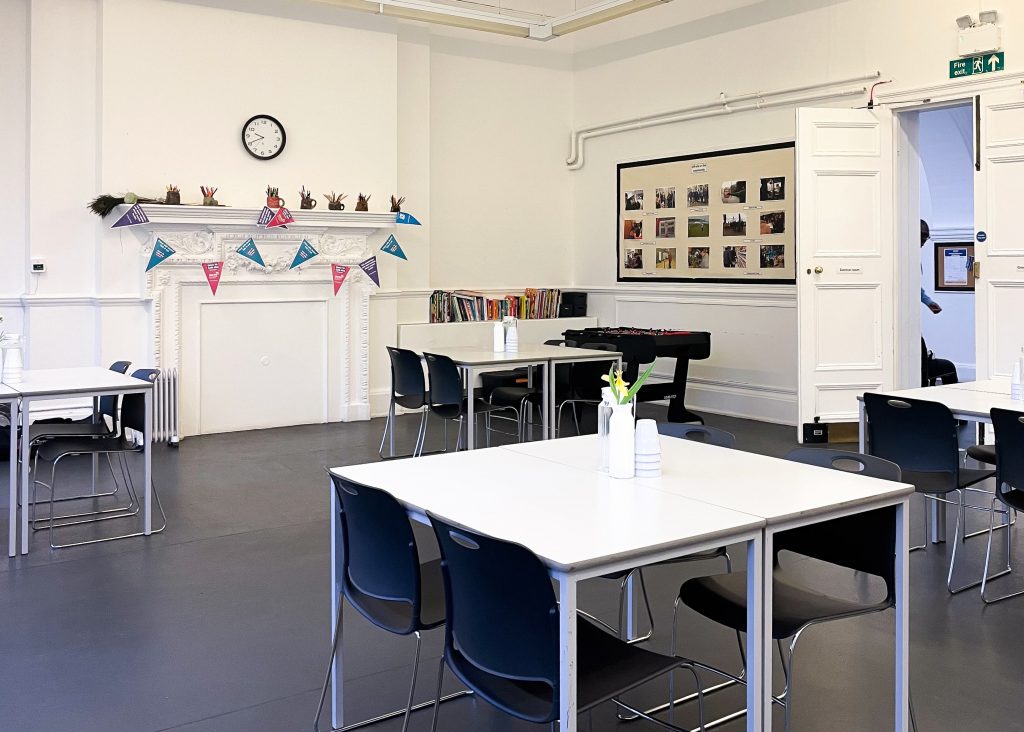 a black-floored room with white tables and black chairs, there is a white fireplace with blue, purple and pink bunting hanging over it