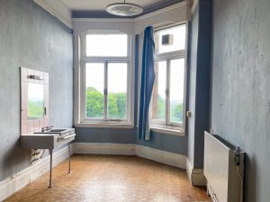brown wooden floored rom with blue walls and a sink with a mirror on one side and windows at the end of the room