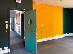 a turquoise door with a circular window inside it. the door enters a room with yellow and turquoise walls