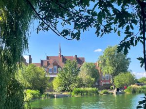 a red brick building surrounded by trees in front of a lake