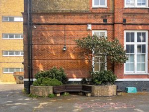 red brick wall with a bench and bushes in front