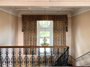 a black banister in a room with a large chandalier and windows