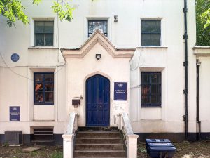 white building exterior with blue door and blue signs with white writing reading 'lowe guardians in residence'