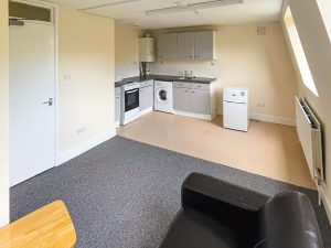 a kitchen lounge room with a kitchen in a corner and a black couch