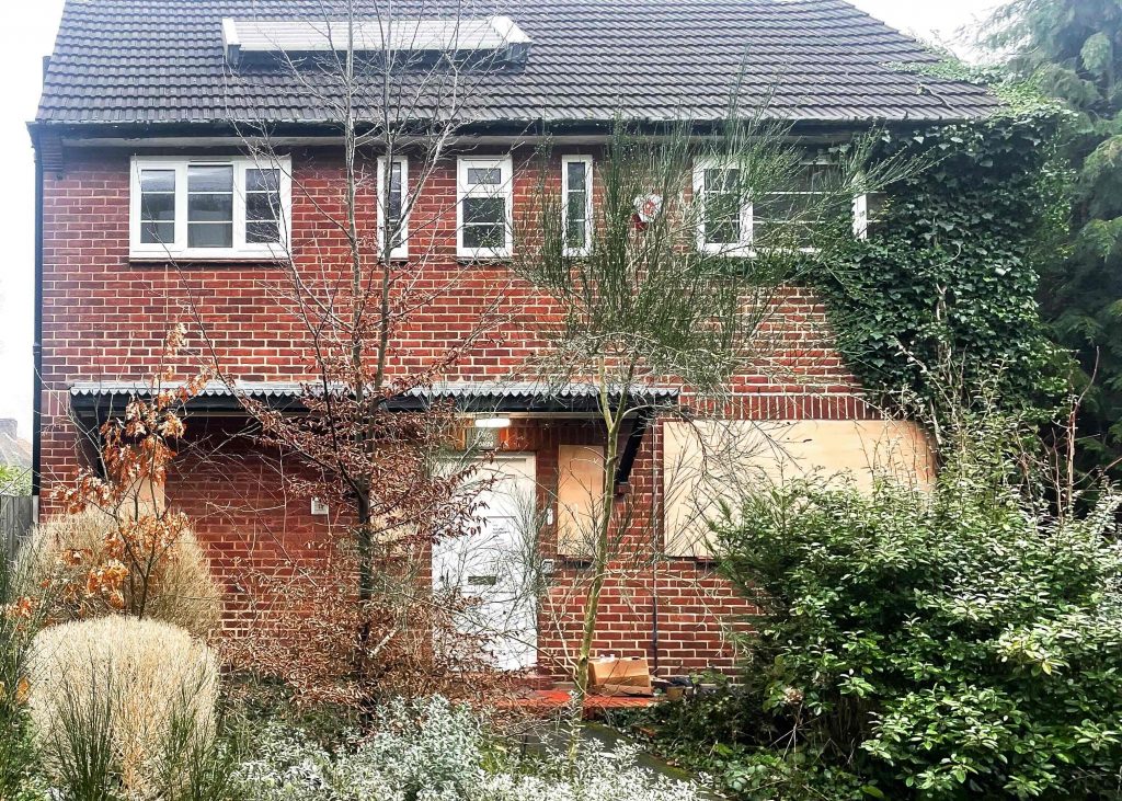 a small red brick cottage with overgrown garden in front