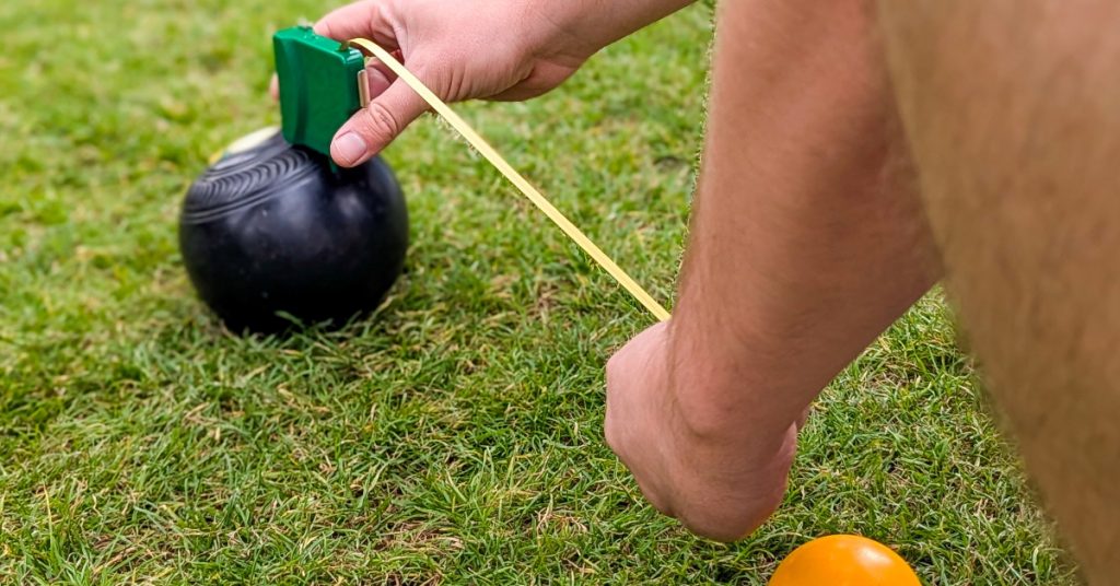 a measuring tape being used to measure the distance between two lawn bowls